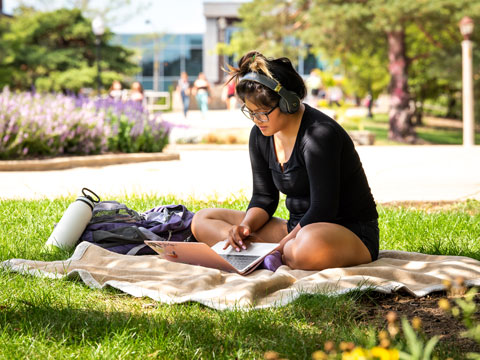 A student studies on the lawn of the quad.