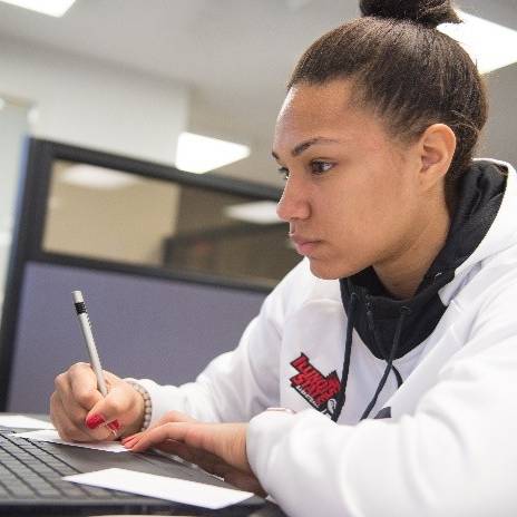 A student carrying taking notes on paper while working on a laptop