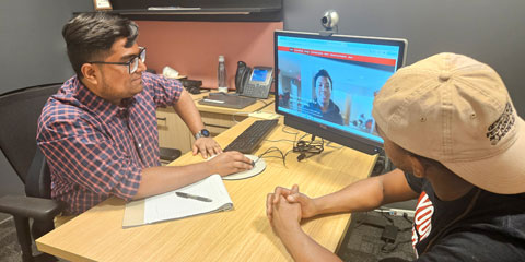 A staff member tutoring a student referencing a desktop computer screen.